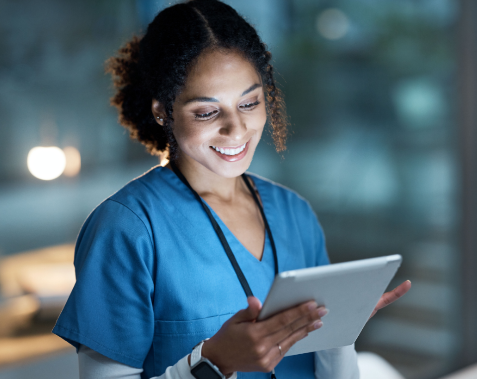 A female healthcare professional in scrubs using a medical tablet.