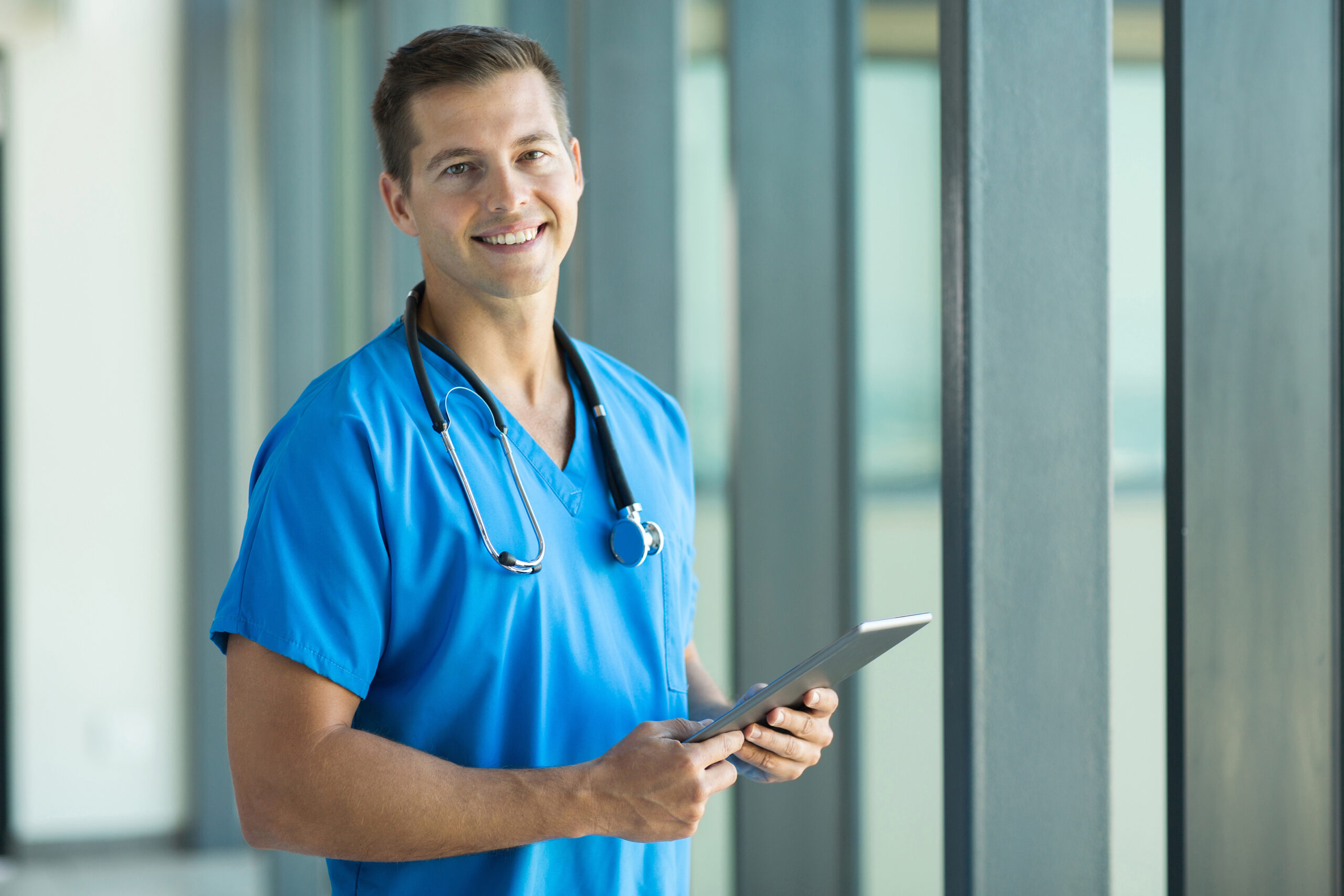 Male doctor in blue scrubs, tablet in hand, ready to care for patients